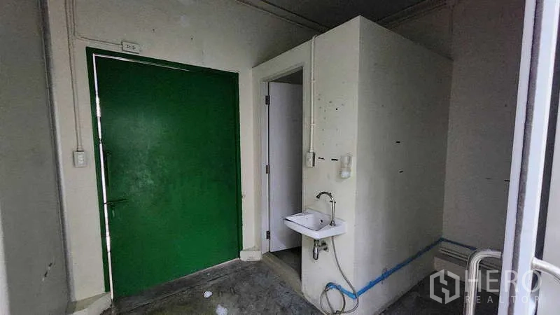 Factory for rent in Samut Sakhon - Service corner with green exit door, sink and attached restroom.