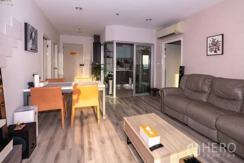 Condominium for rent in Sathon, Bangkok - Bright living and dining area with leather sofa, wood floors, and a glass-partition kitchen.