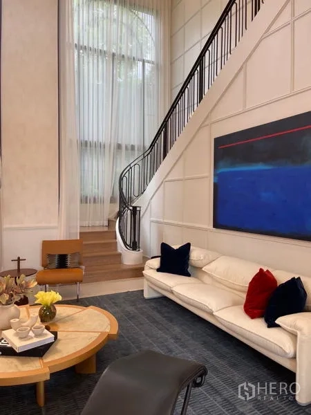 Detached House for sale in Suan Luang, Bangkok - Cozy lounge corner with tall curtains, abstract artwork and stairs to the upper floor.