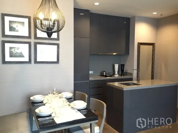 Condominium for rent in Bang Rak, Bangkok - Modern grey kitchen with stone island and a cozy dining nook set for four beneath a sculptural pendant lamp.