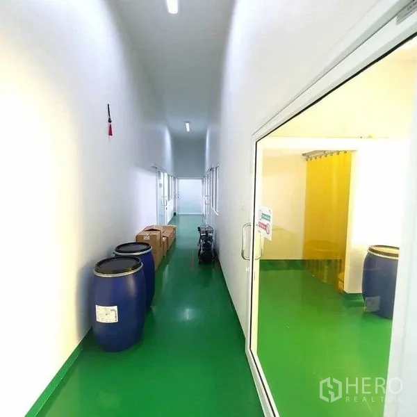 工厂 出售在Bang Pa-in, Phra Nakhon Si Ayutthaya - 明亮走廊摆放蓝色桶和纸箱，右侧为黄帘房间入口。