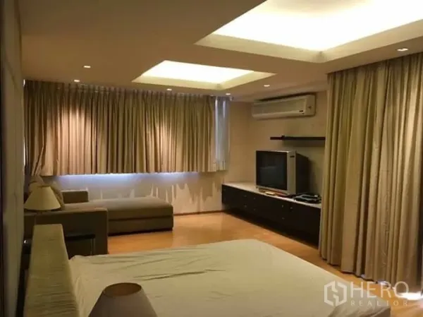 Condominium for rent in Watthana, Bangkok - Large master bedroom with TV console, sofa, full-length curtains, wood floors, and cove lighting.