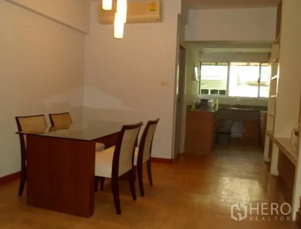 Condominium for rent in Pathum Wan, Bangkok - Dining area with a glass-top table for four, pendant lighting, and access to a bright kitchen with large window.