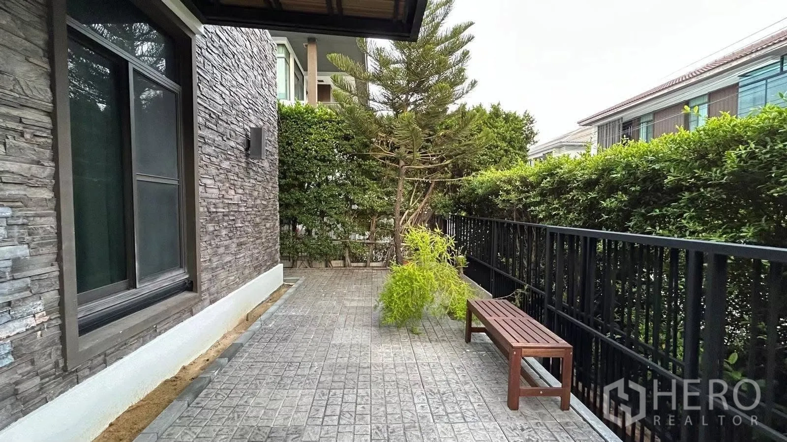 บ้านเดี่ยว for rent in Prawet, Bangkok - ลานข้างบ้านปูกระเบื้อง ผนังหินเทียม รั้วพุ่มไม้ และม้านั่งไม้