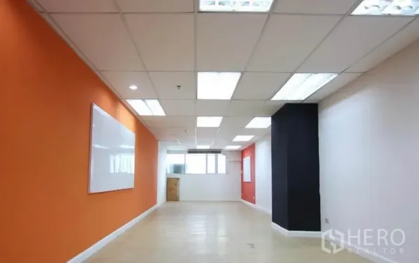 办公空间 出租在Watthana, Bangkok - 细长培训室，橙色点缀墙、白板与明亮顶灯。