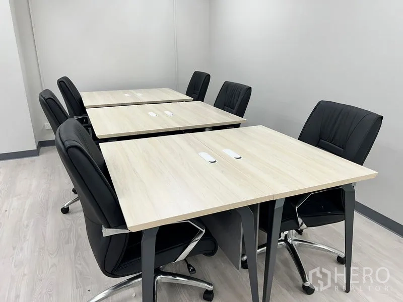 Office Space for rent in Sathon, Bangkok - Close-up of paired light-wood workstations with black ergonomic chairs on casters.