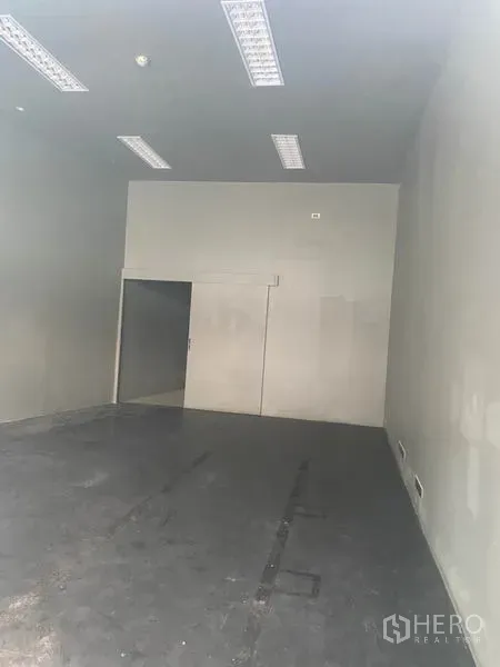 零售空间 出租在Khlong Toei, Bangkok - 空置商铺内部，高挑层高、荧光灯与水泥地面。