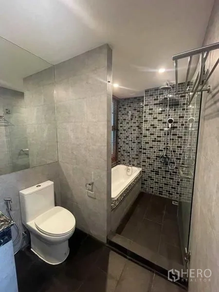 Condominium for rent in Watthana, Bangkok - Second bathroom with bathtub, walk-in shower with mosaic wall, toilet and large mirror.