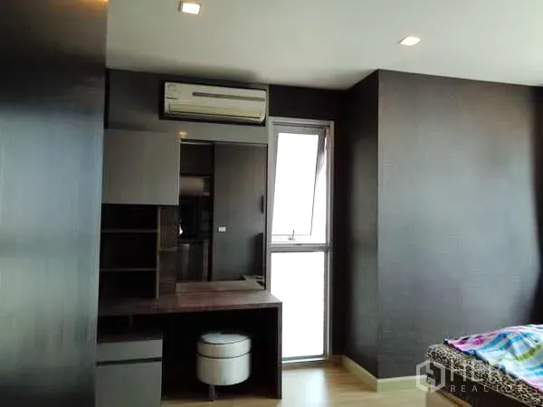 公寓 出租在Watthana, Bangkok - 主卧带梳妆台、空调与转角窗，深色特色墙面。