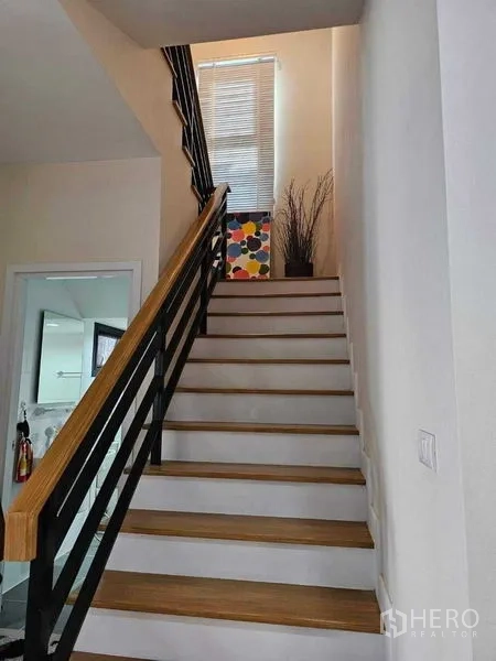 独立式住宅 出售在Khan Na Yao, Bangkok - 木踏板楼梯与黑色栏杆，通往二楼，采光良好。