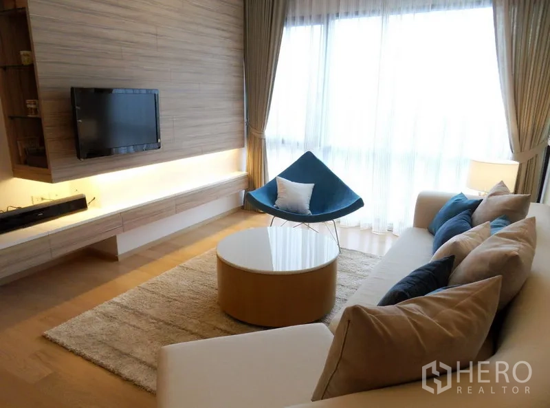 คอนโด ให้เช่าในPhaya Thai, Bangkok - ห้องนั่งเล่นสว่าง โซฟา ผนังทีวี โต๊ะกาแฟกลม และหน้าต่างสูงพร้อมม่านโปร่ง