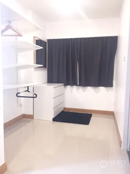 Condominium for rent in Watthana, Bangkok - White walk-in closet area featuring open shelves, hanging rail, chest of drawers, and a window with dark curtains.