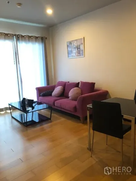 公寓 出租在Khlong San, Bangkok - 明亮客厅，紫色沙发、抱枕、玻璃茶几与落地窗帘。