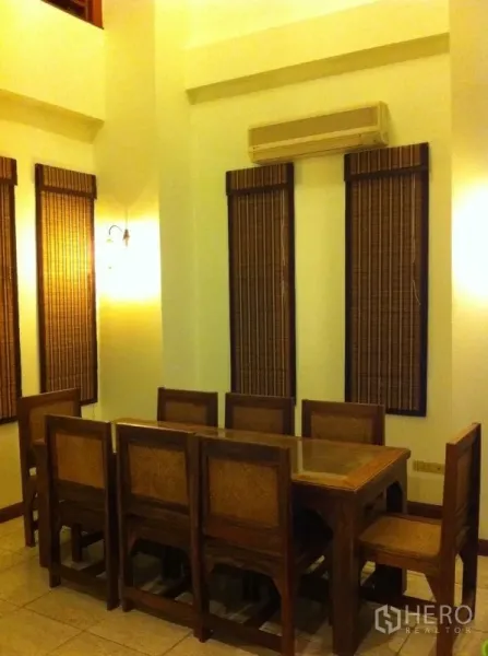 Townhouse for rent or sale in Watthana, Bangkok - Dining area with a long wooden table, high ceiling and air conditioning.