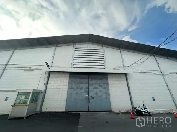 คลังสินค้า ให้เช่าในKhlong Toei, Bangkok - ด้านหน้าโกดัง ประตูเหล็กบานคู่ขนาดใหญ่ ผนังระบายอากาศ และป้อมยามขนาดเล็ก.