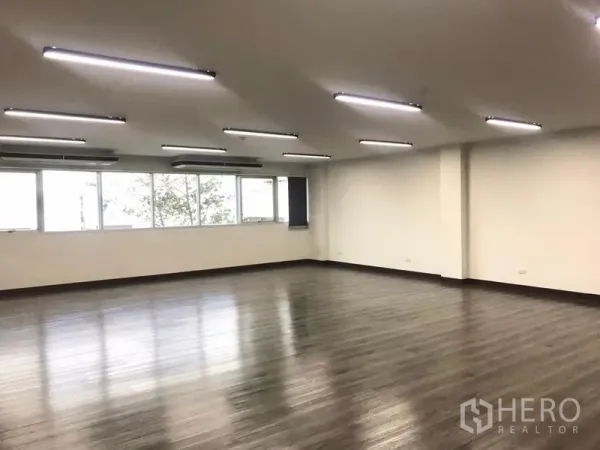 Office Space for rent in Bangkok Noi, Bangkok - Corner view showing long window wall, ceiling AC units, and smooth vinyl flooring.