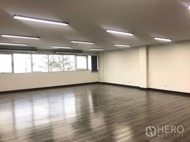 Office Space for rent in Bangkok Noi, Bangkok - Corner view showing long window wall, ceiling AC units, and smooth vinyl flooring.