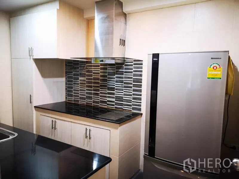 Townhouse for rent in Suan Luang, Bangkok - Built-in kitchen with cooktop, stainless hood, tiled backsplash and large refrigerator.
