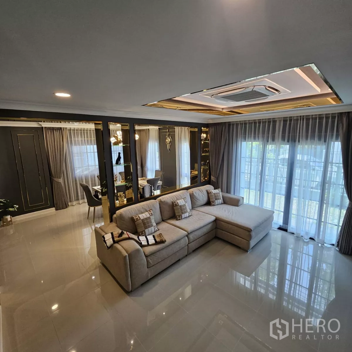 Detached House for rent in Bang Phli, Samut Prakan - Spacious living room with L-shaped sofa, floor-to-ceiling curtains, glossy tiles and recessed ceiling air-conditioner.