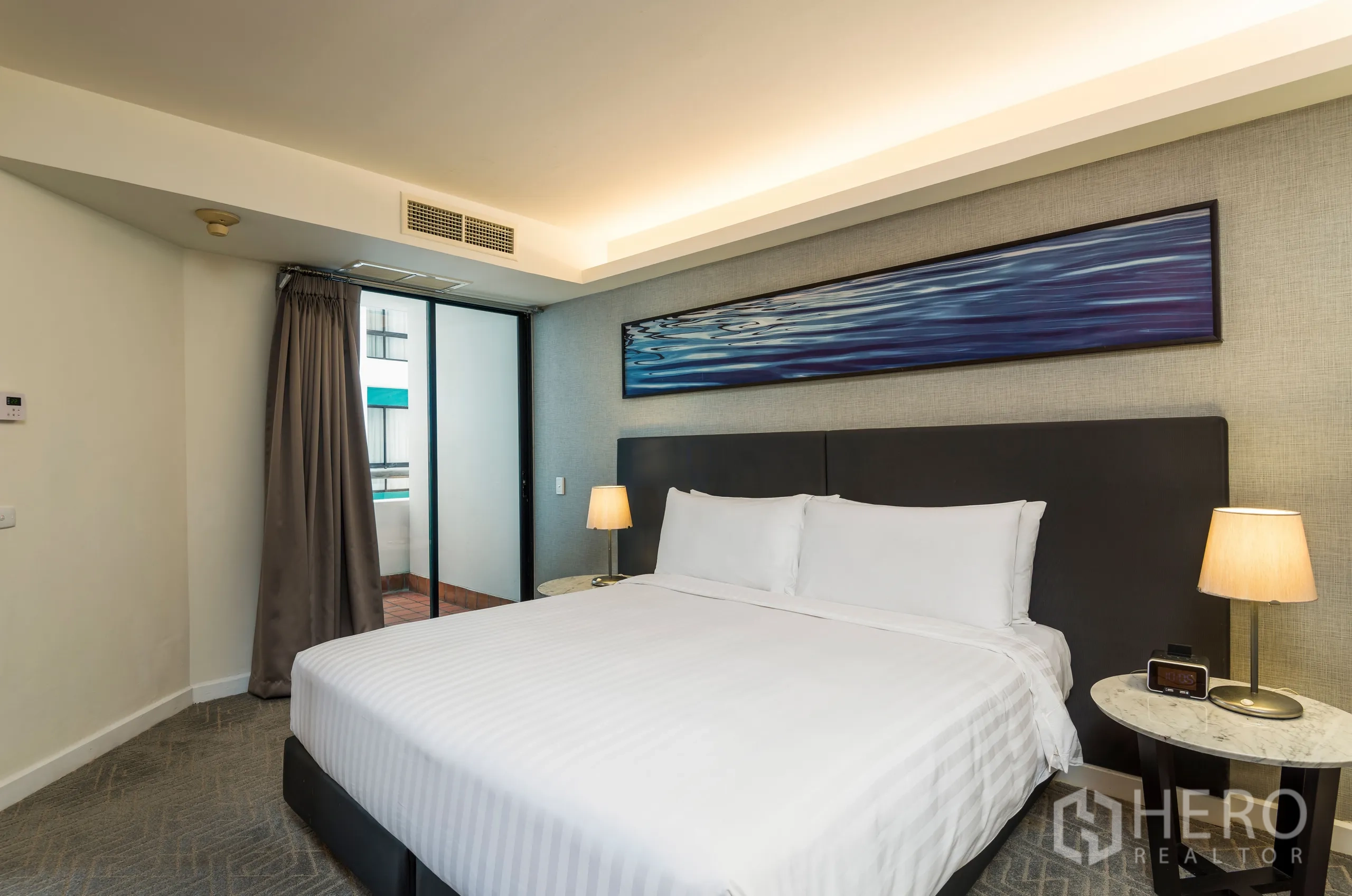 Condominium for rent in Yan Nawa, Bangkok - Bedroom with king bed, bedside lamps, wide headboard art and sliding door to a small balcony.