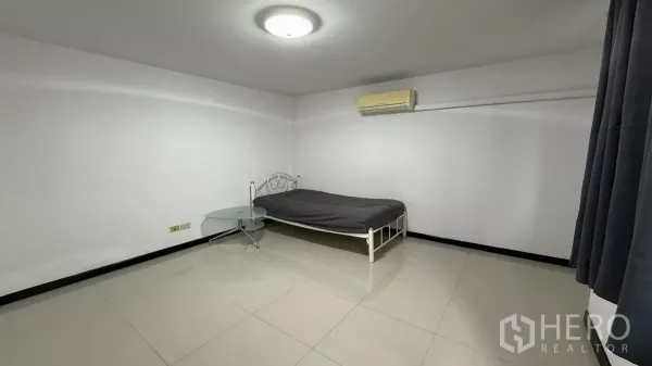 带办公室的家 出租在Bang Na, Bangkok - 极简卧室，单人金属床、圆形玻璃边几、空调与瓷砖地面。