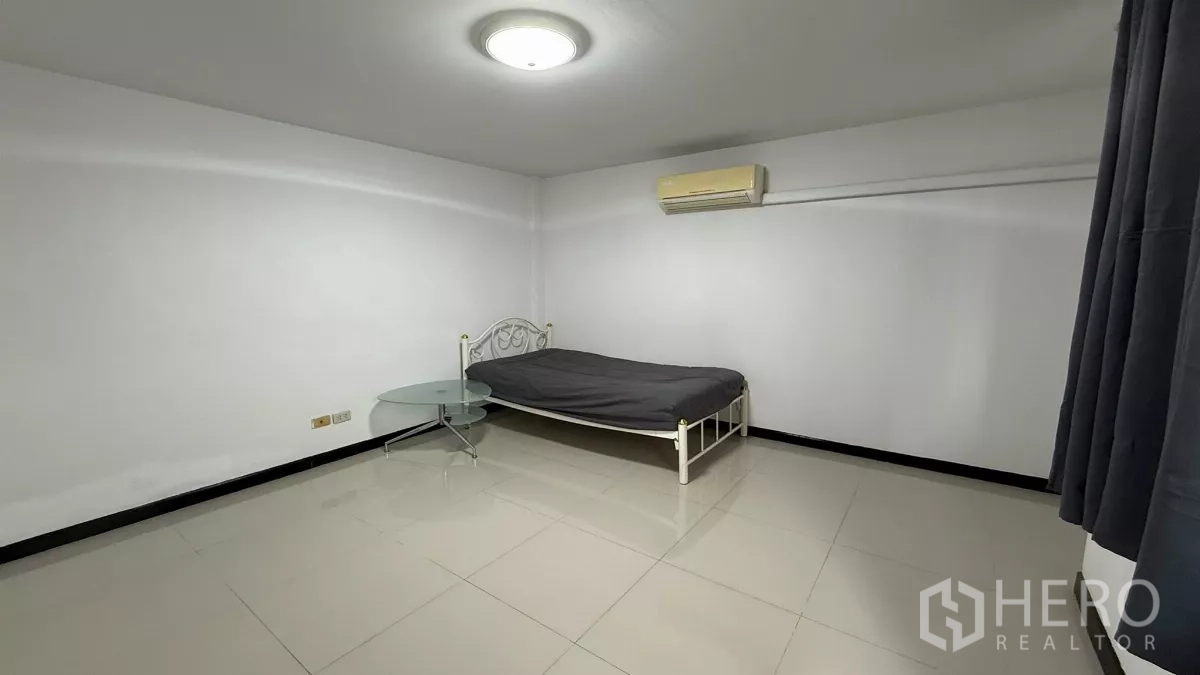 带办公室的家 出租在Bang Na, Bangkok - 极简卧室，单人金属床、圆形玻璃边几、空调与瓷砖地面。