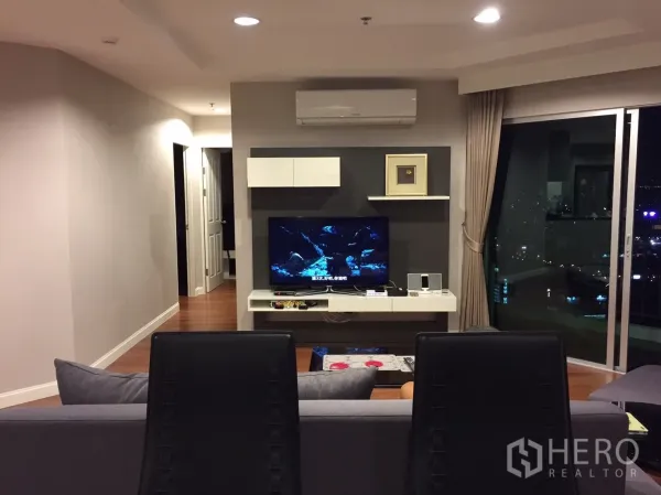 Condominium for rent in Huai Khwang, Bangkok - Living area facing the TV and sliding glass door with night city views.