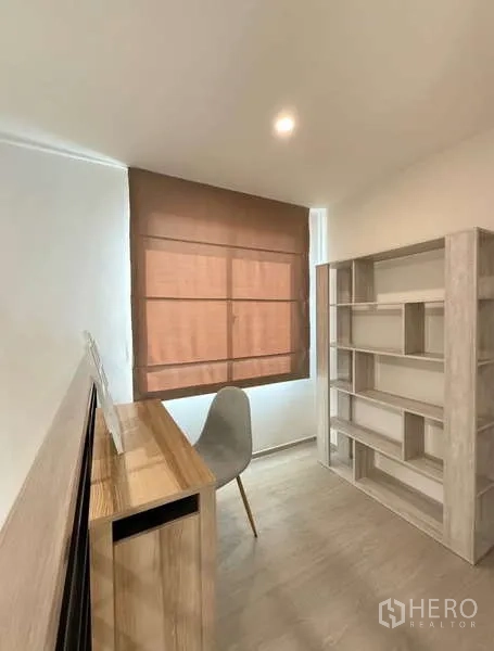 联排别墅 出租在Bang Phli, Samut Prakan - 紧凑书房，木质书桌、灰色椅子与开放式书架，棕色百叶帘。