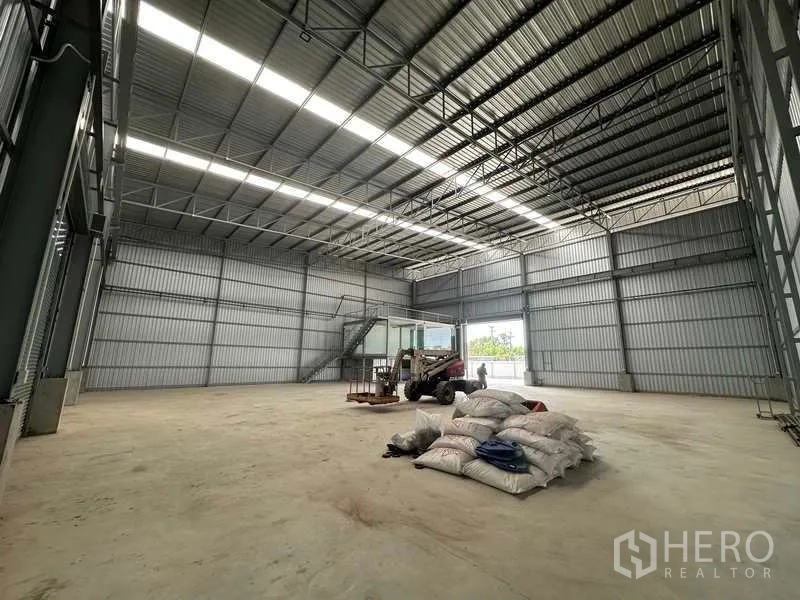 工厂 出租在Wang Noi, Phra Nakhon Si Ayutthaya - 大型存储区，高桁架屋顶，卷帘门打开，地面放置材料。
