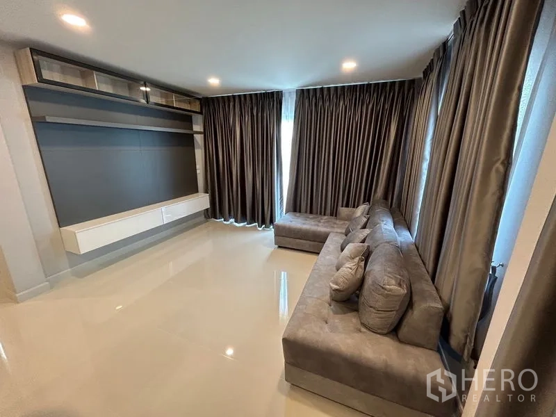 Detached House for rent in Bang Phli, Samut Prakan - Living room with L-shaped gray sofa and built-in media wall.