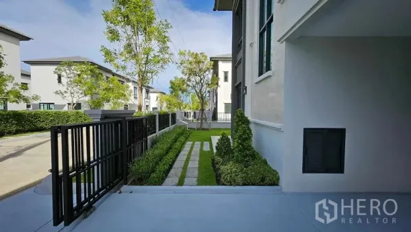 Detached House for sale in Samut Prakan - Front yard with metal gate, manicured hedges, and walkway beside the modern house.