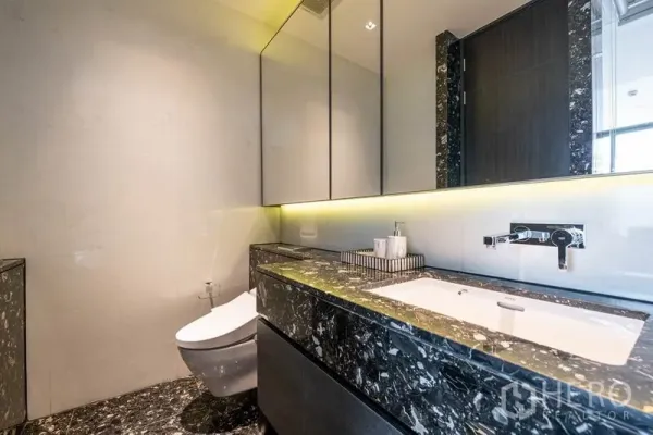 Condominium for rent or sale in Khlong Toei, Bangkok - Modern bathroom with backlit mirror, marble vanity and wall-hung toilet.
