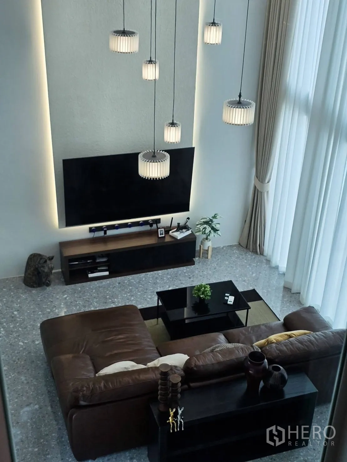 Detached House for rent in Suan Luang, Bangkok - High-ceiling living room with sectional sofa, TV wall and tall curtains.
