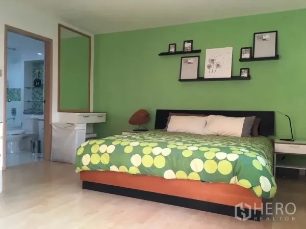 คอนโด ให้เช่าในPathum Wan, Bangkok - ห้องนอนหลักผนังสีเขียว เตียงคิงไซส์ ชั้นวางลอย และทางเข้าห้องน้ำ