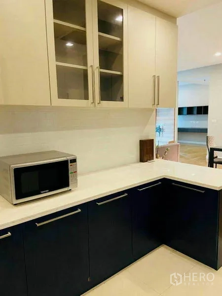 Condominium for rent in Watthana, Bangkok - Modern U-shaped kitchen with two-tone cabinets, white countertops, and a microwave.