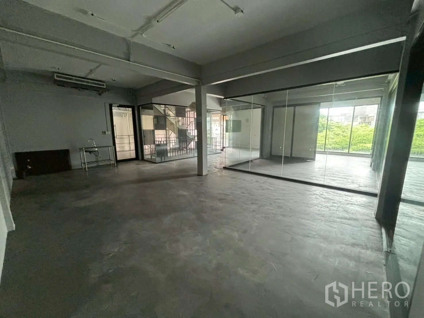 สำนักงาน ให้เช่า - พื้นที่สำนักงานแบบเปิดกว้าง พื้นคอนกรีต ห้องประชุมกั้นกระจกและหน้าต่างมองวิวต้นไม้.