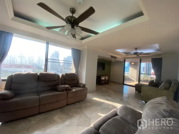 Condominium for rent or sale in Watthana, Bangkok - Sunlit living room with ceiling fans, large sofas and sliding doors to the terrace with city views.