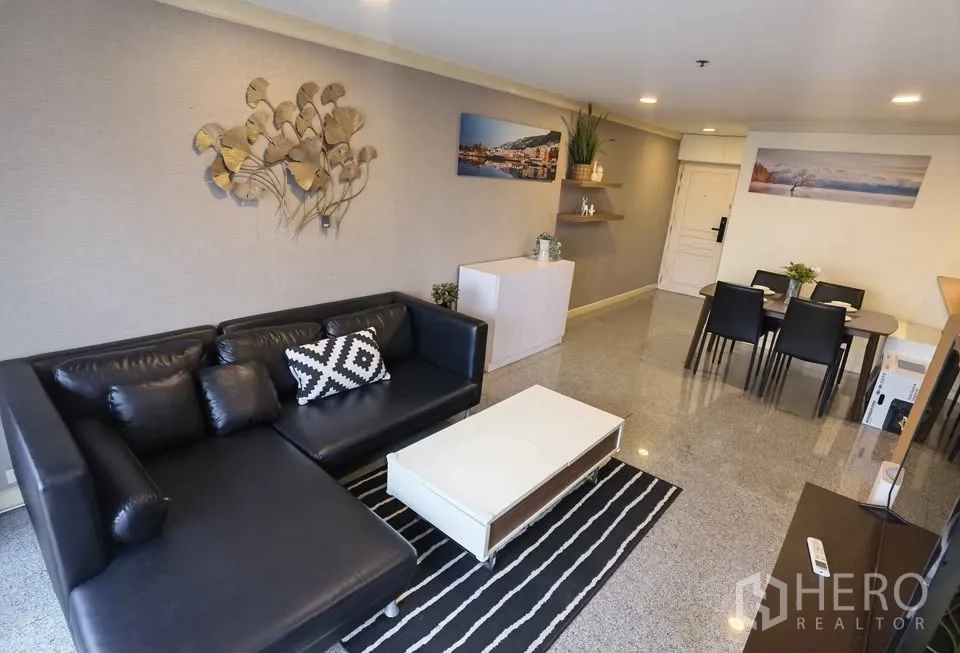 Condominium for rent in Khlong Toei, Bangkok - Open living and dining area with black L-shaped sofa and coffee table.