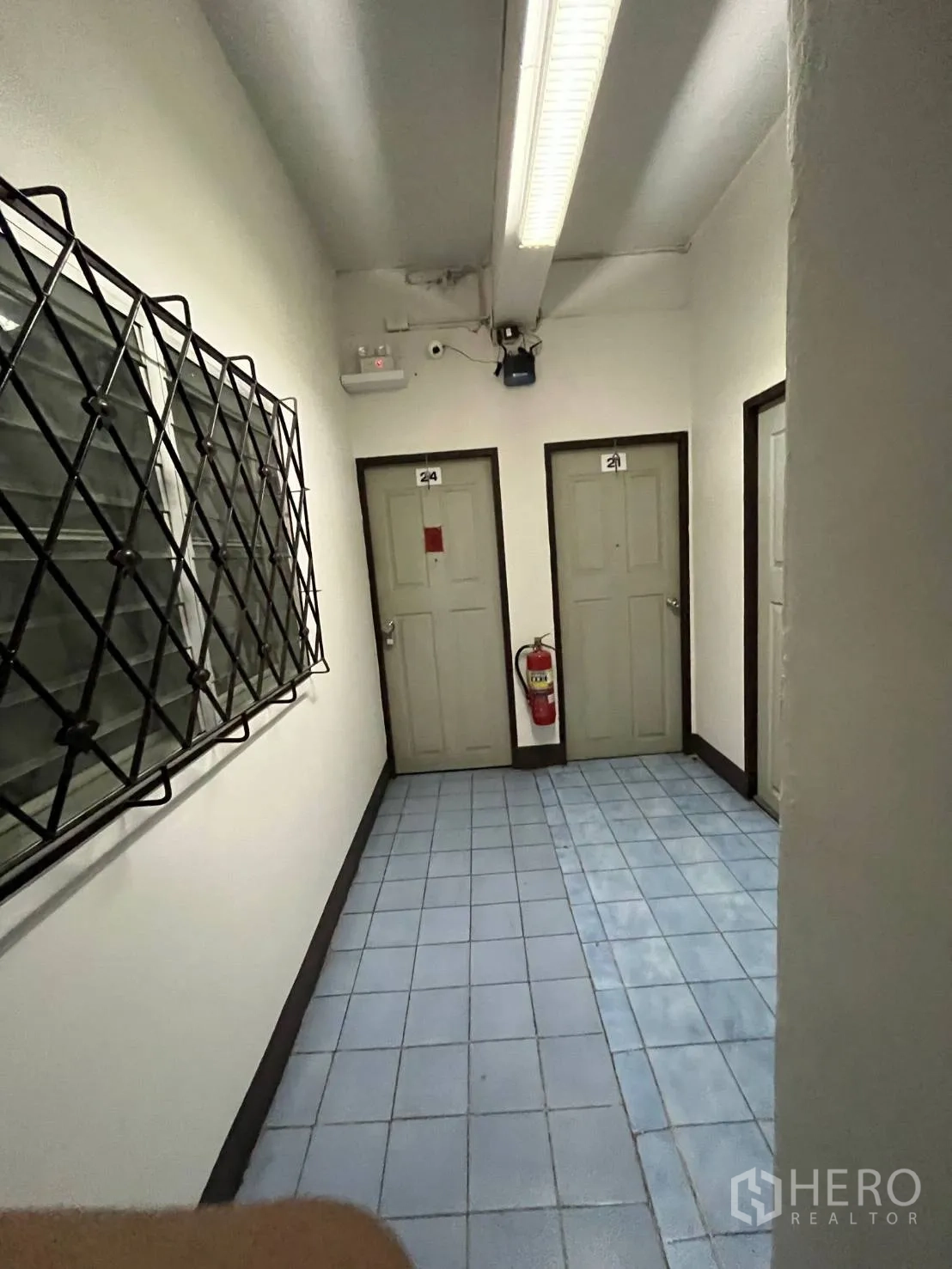 Shophouse for rent in Khlong Toei, Bangkok - Tiled corridor with three numbered doors, barred window, and a wall-mounted fire extinguisher.