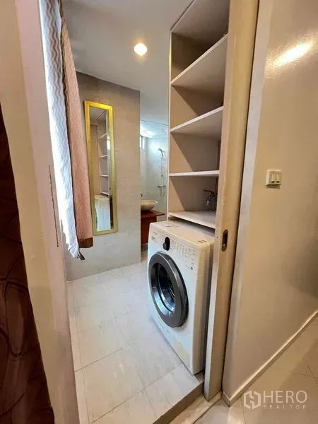 Condominium for rent in Ratchathewi, Bangkok - Compact laundry nook with front‑load washer and open shelving beside the bathroom.