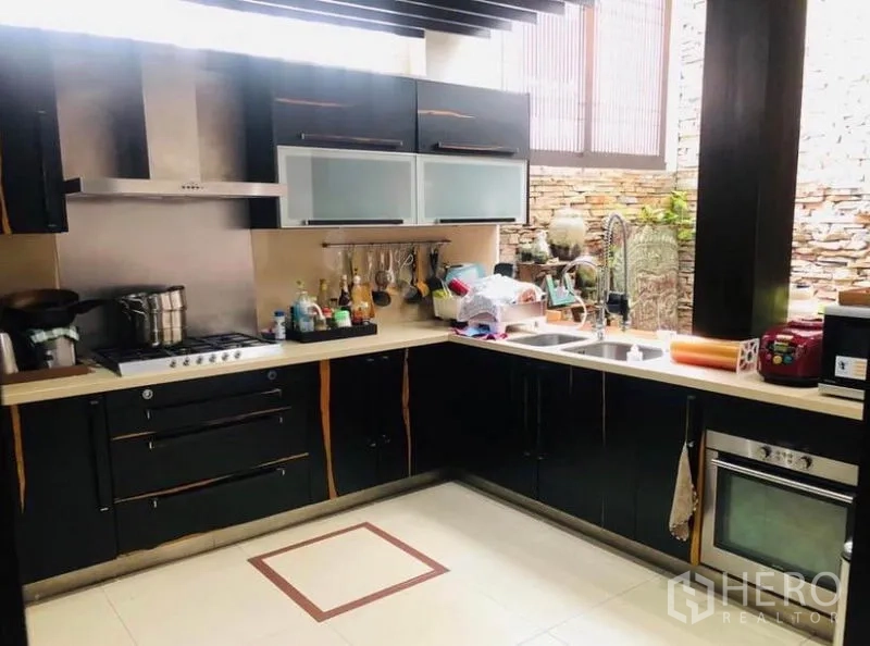 Condominium for rent in Pathum Wan, Bangkok - Modern L-shaped kitchen with black cabinetry, stainless range hood and stone-clad window feature.
