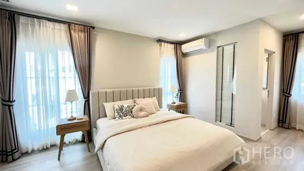 Detached House for rent or sale in Prawet, Bangkok - Bright master bedroom with upholstered bed, bedside tables, curtains and ensuite access.