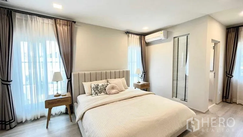 Detached House for rent or sale in Prawet, Bangkok - Bright master bedroom with upholstered bed, bedside tables, curtains and ensuite access.