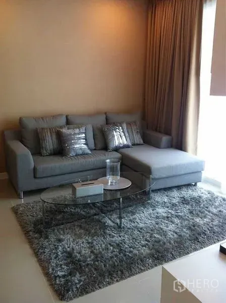 公寓 出售在Ratchathewi, Bangkok - 现代客厅，灰色转角沙发、长绒地毯与玻璃茶几，落地窗帘旁。