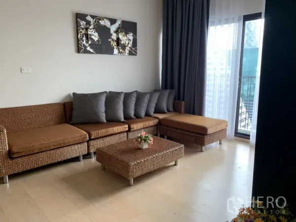 公寓 出租在Phaya Thai, Bangkok - 明亮客厅，藤编转角沙发与茶几，浅木地板，带窗帘的阳台推拉门。