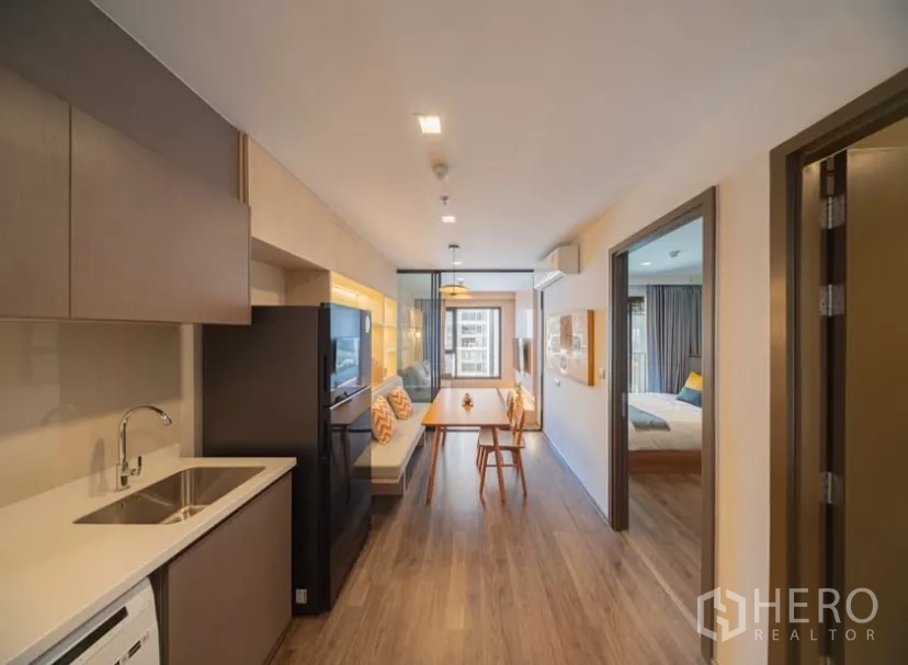 คอนโด ให้เช่าในChatuchak, Bangkok - ครัวเปิดพร้อมท็อปสีขาว โต๊ะทานอาหาร และประตูกระจกกั้นพื้นที่ไปยังห้องนั่งเล่นในคอนโดจตุจักร