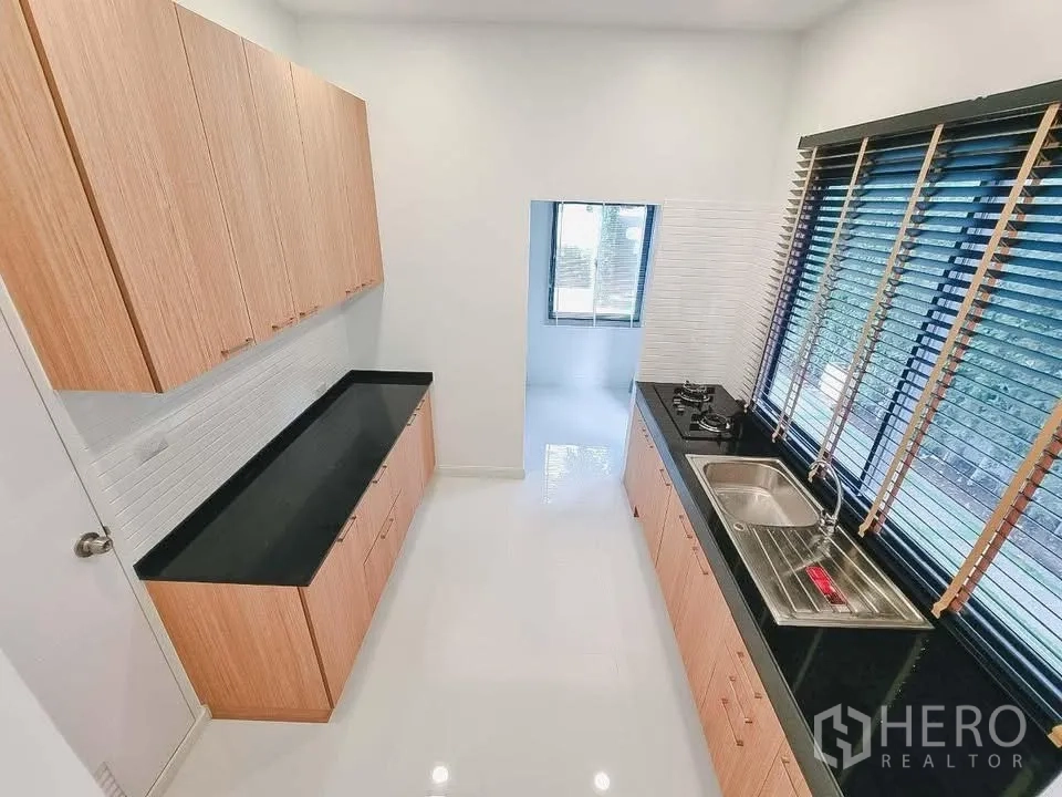 Detached House for rent or sale in Bang Phli, Samut Prakan - Separate kitchen with long black countertop, sink, gas hob, and wood cabinets.