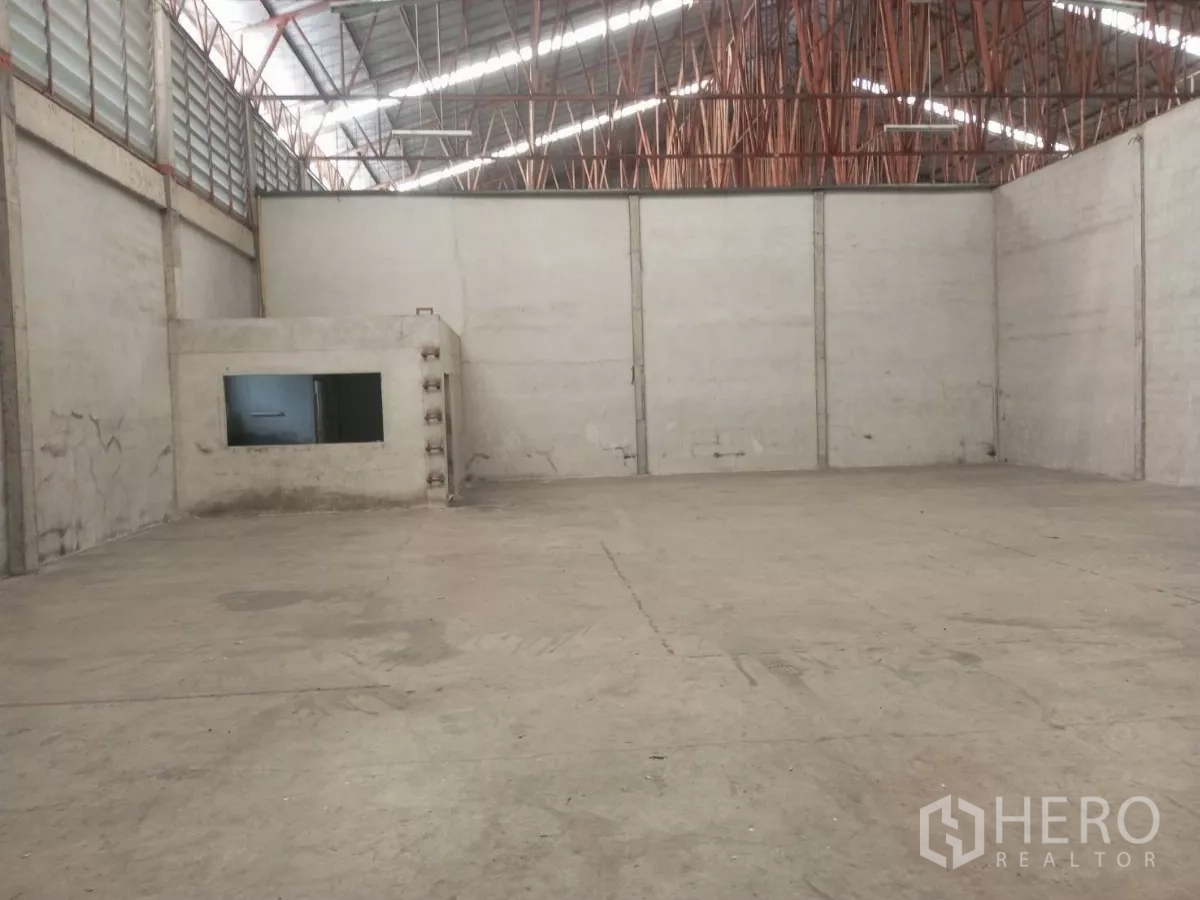 Warehouse for rent in Min Buri, Bangkok - Spacious warehouse floor with steel roof trusses and a built-in office corner.