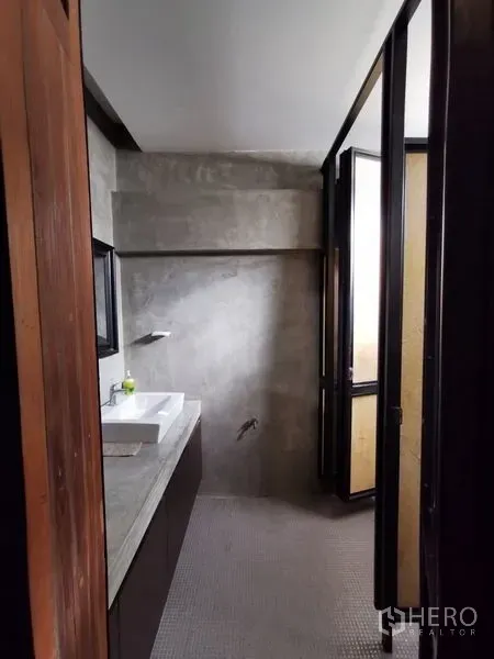 Home Office for sale in Wang Thonglang, Bangkok - Compact bathroom with concrete walls, white basin and a door opening to natural light.