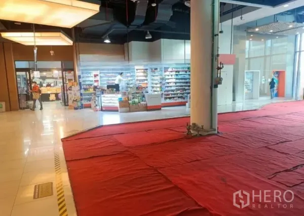 Retail Space for rent in Khlong Toei, Bangkok - Corner retail unit with floor-to-ceiling glass frontage, high black ceiling, central pillar and red protective flooring inside a shopping mall.